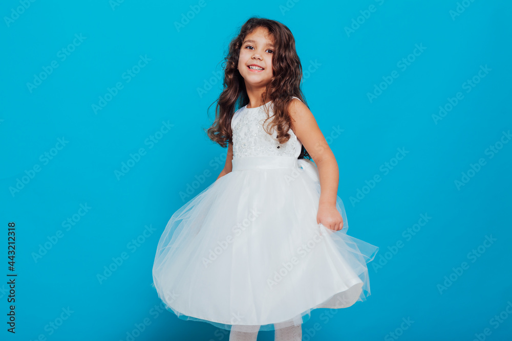 Beautiful little curly girl 5 years old in a white dress on a blue background Beautiful little curly girl 5 years old in a white dress on a blue background