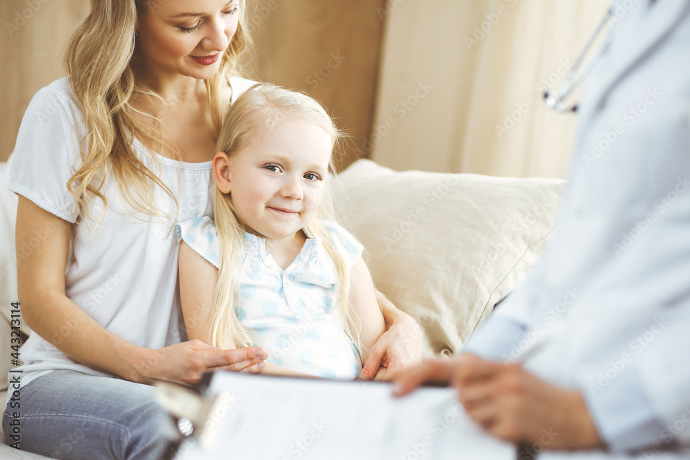 Doctor and patient. Pediatrician using clipboard while examining little girl with her mother at home. Happy cute caucasian child at medical exam. Medicine concept Doctor and patient. Pediatrician using clipboard while examining little girl with her mother at home. Happy cute caucasian child at medical exam. Medicine concept