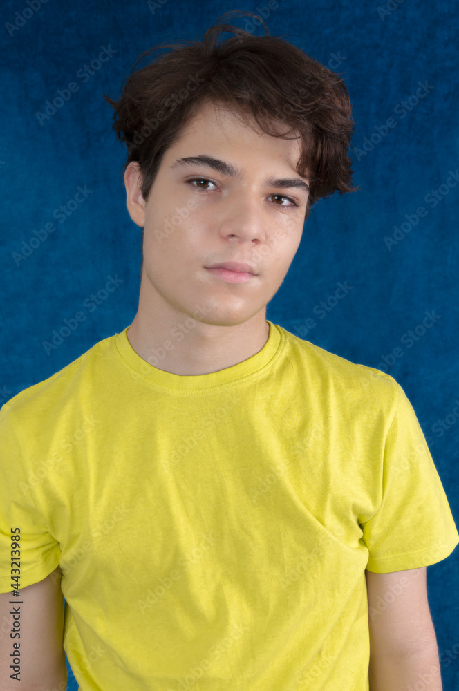 Young man looking at camera in yellow shirt, brown hair isolated on blue background Young man looking at camera in yellow shirt, brown hair isolated on blue background