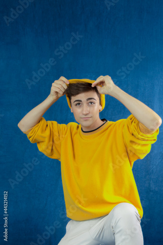 young caucasian man playing with his yellow cap isolated on blue background