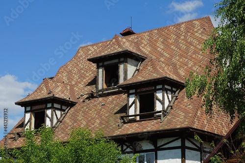 attic of an old abandoned private house with an empty windows under a brown tiled roof against a blue sky
