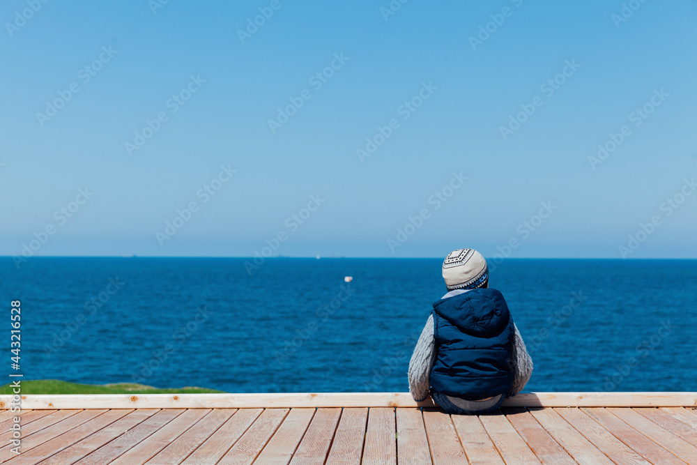 Little boy sits alone and looks at the ships in the sea