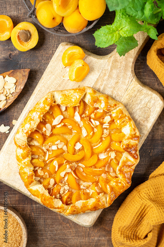 Foto French Galette or a pie with apricots and almonds on on a wooden serving board on a brown culinary background top view