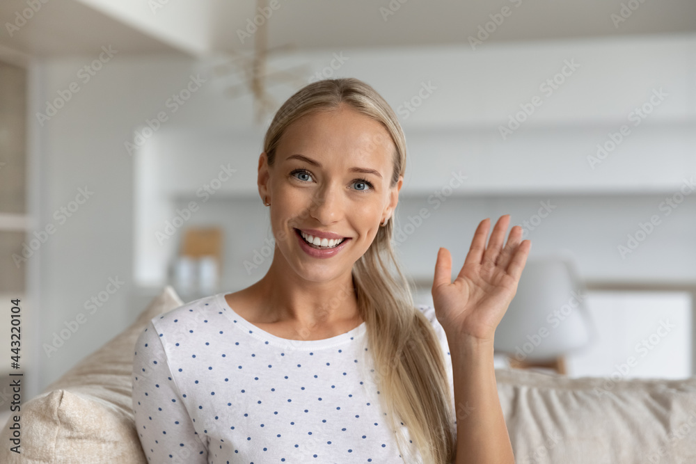 Head shot portrait of smiling woman waving hand and looking at camera, making video call chatting online greeting friends or viewers sitting on couch at home, happy popular blogger recording content Head shot portrait of smiling woman waving hand and looking at camera, making video call chatting online greeting friends or viewers sitting on couch at home, happy popular blogger recording content