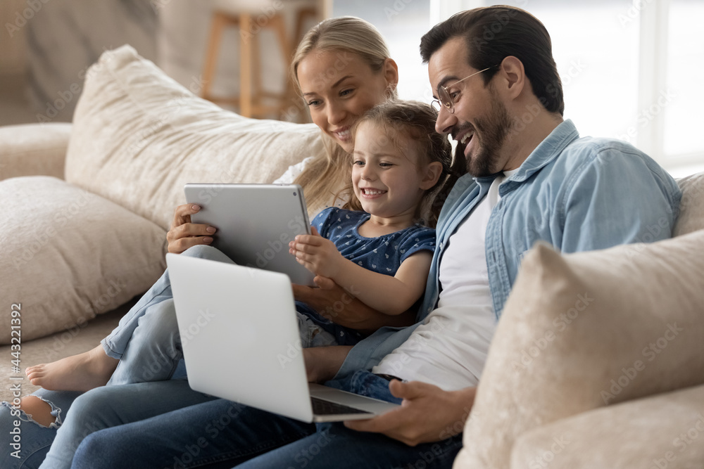 Happy family with little daughter having fun with modern devices, sitting on cozy couch together, smiling mother and father with adorable child girl looking at tablet screen, watching funny video Happy family with little daughter having fun with modern devices, sitting on cozy couch together, smiling mother and father with adorable child girl looking at tablet screen, watching funny video
