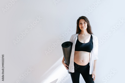Pregnant woman posing for a photo with yoga mat in hand