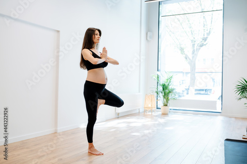 Peaceful pregnant woman balancing on one leg  practicing yoga alone in a studio