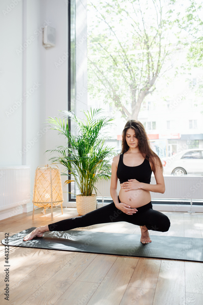 Sensual pregnant woman sitting in a side lunge, practicing yoga alone Sensual pregnant woman sitting in a side lunge, practicing yoga alone