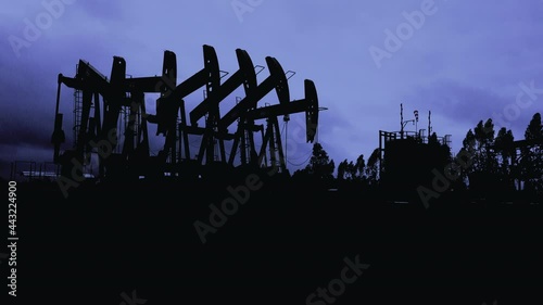 Silhouette of oil extracting operation by pump jack in the oil field
