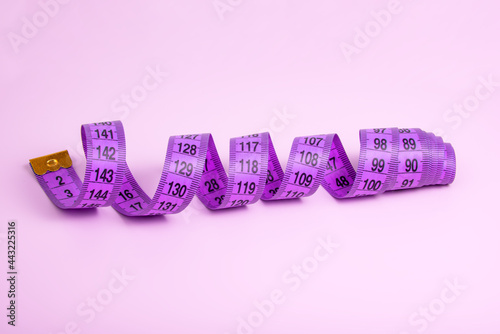Bright purple tape measure on violet background with copyspace