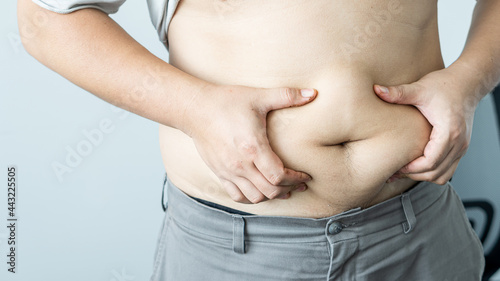 Close-up of an overweight fat man's hand grabbing his huge belly and looking at the huge belly hanging out of his pants after a fast-food dinner.