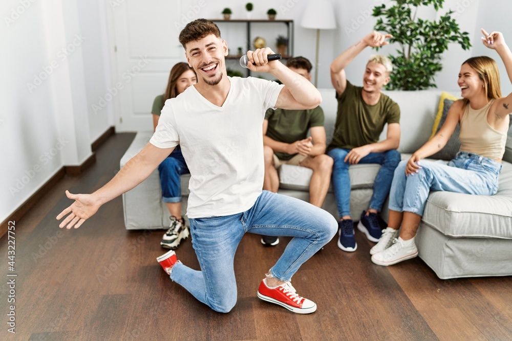 Group of young friends having party singing song using microphone at home.