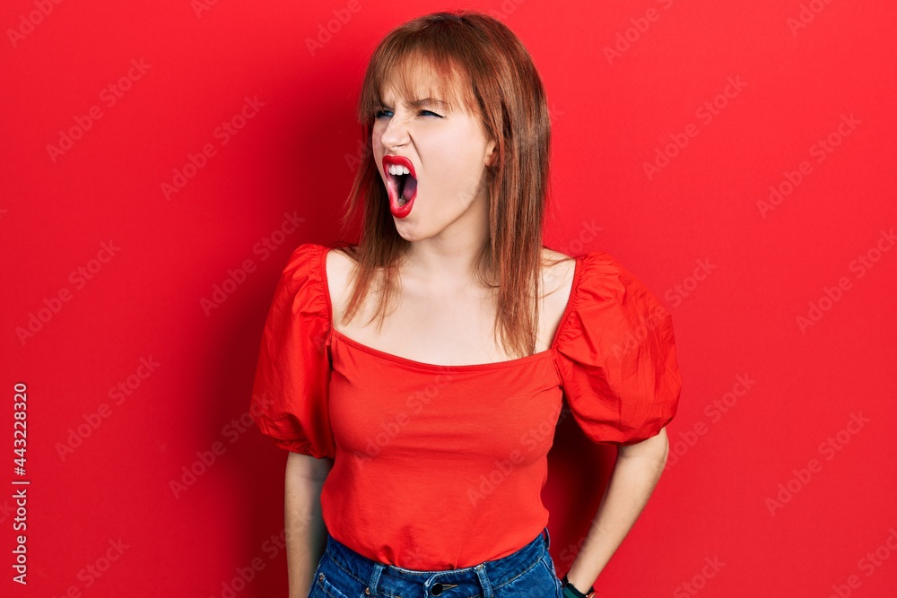 Redhead young woman wearing casual red t shirt angry and mad screaming frustrated and furious, shouting with anger. rage and aggressive concept. Redhead young woman wearing casual red t shirt angry and mad screaming frustrated and furious, shouting with anger. rage and aggressive concept.