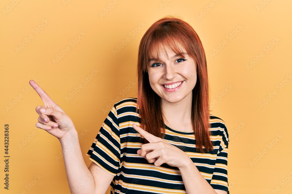 Redhead young woman wearing casual striped t shirt smiling and looking at the camera pointing with two hands and fingers to the side. Redhead young woman wearing casual striped t shirt smiling and looking at the camera pointing with two hands and fingers to the side.