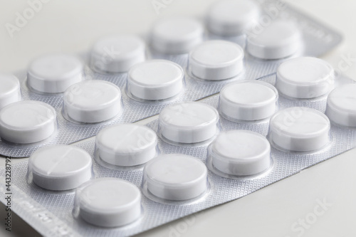 round white pills in a blister on a white table close-up, macro medical background