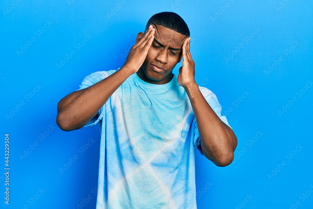 Young black man wearing tye die t shirt suffering from headache desperate and stressed because pain and migraine. hands on head. Young black man wearing tye die t shirt suffering from headache desperate and stressed because pain and migraine. hands on head.