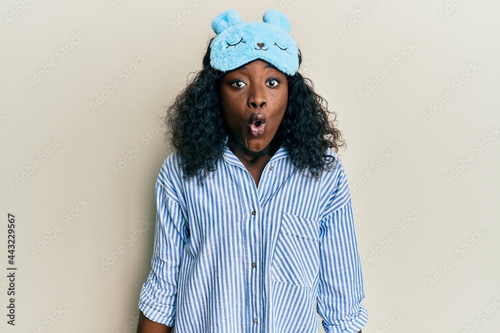 Beautiful african young woman wearing sleep mask and pajama scared and amazed with open mouth for surprise, disbelief face Beautiful african young woman wearing sleep mask and pajama scared and amazed with open mouth for surprise, disbelief face