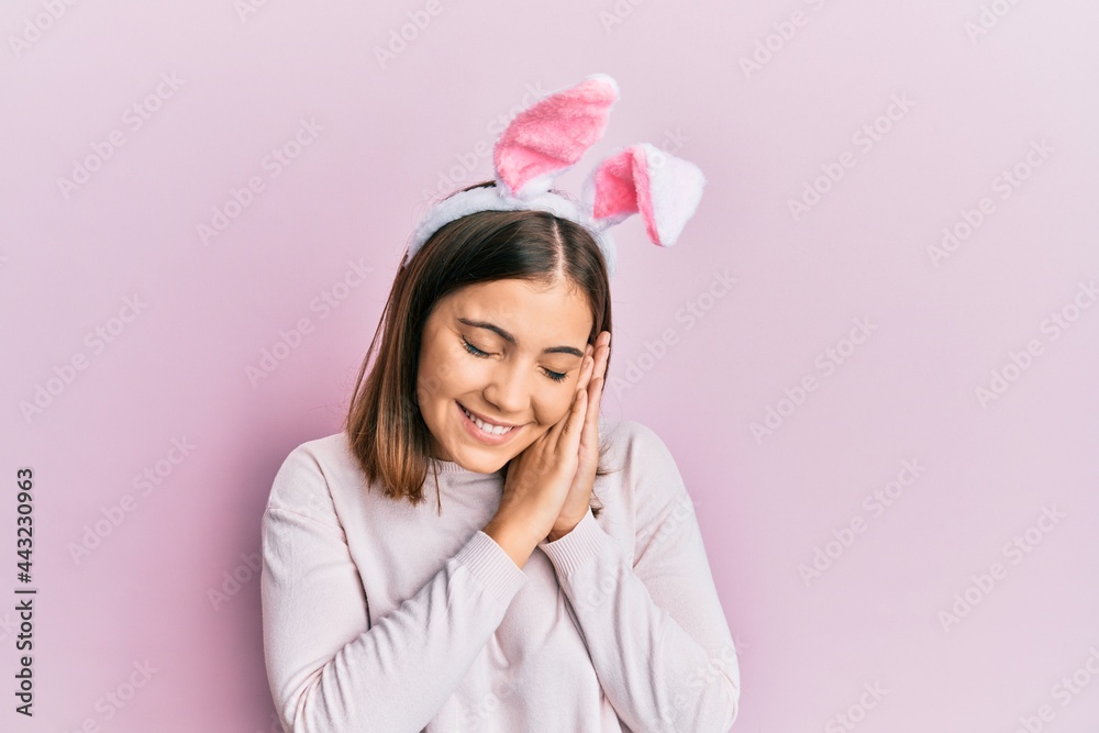 Young beautiful woman wearing cute easter bunny ears sleeping tired dreaming and posing with hands together while smiling with closed eyes. Young beautiful woman wearing cute easter bunny ears sleeping tired dreaming and posing with hands together while smiling with closed eyes.