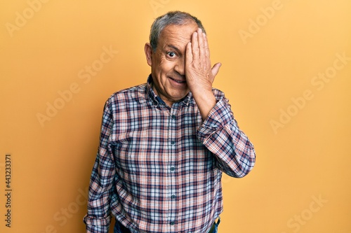 Handsome senior man with grey hair wearing casual shirt covering one eye with hand, confident smile on face and surprise emotion. © Krakenimages.com