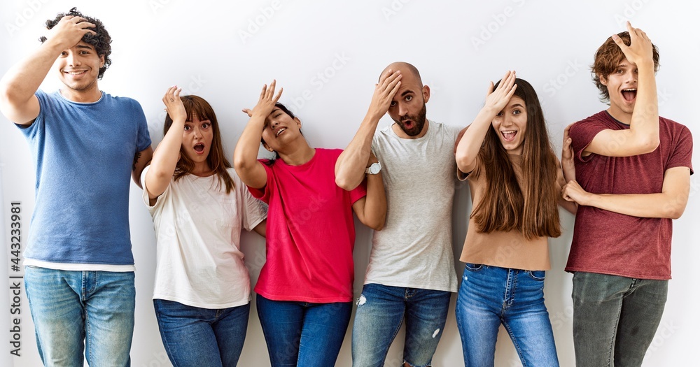 Fototapeta premium Group of young friends standing together over isolated background surprised with hand on head for mistake, remember error. forgot, bad memory concept.