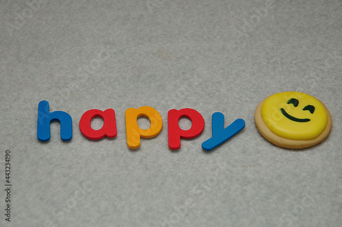A smiley emoji biscuit with the word happy on a white background