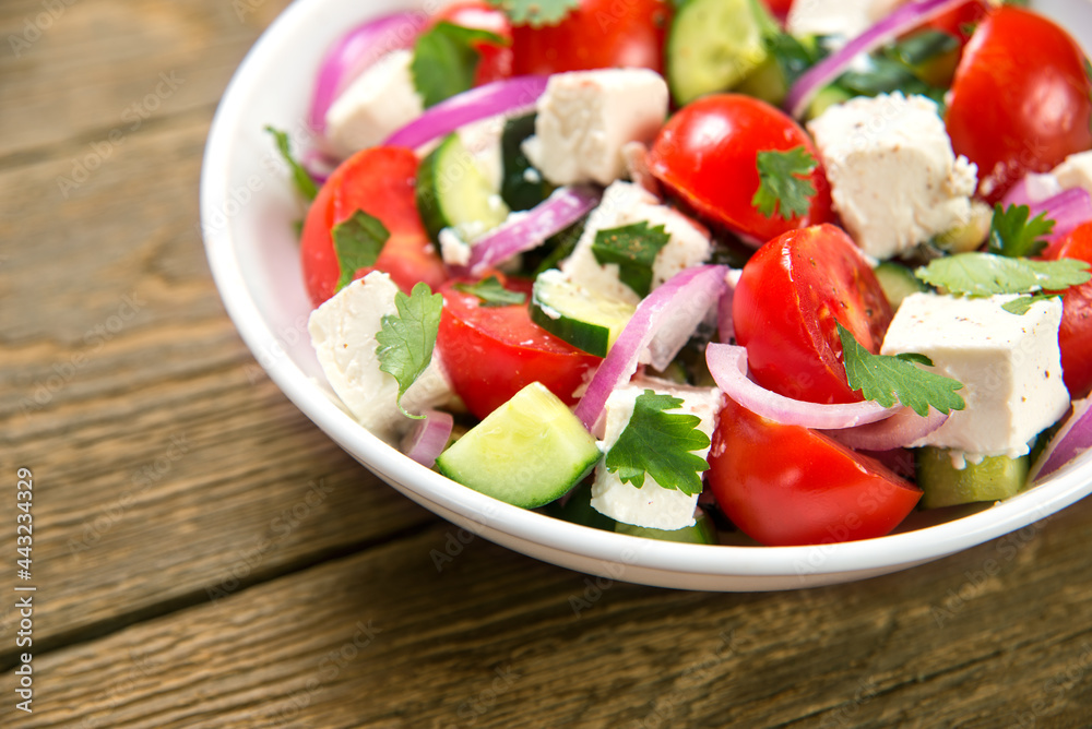 Salad with fresh tomatoes, cucumbers, red onions and feta cheese in a white salad bowl on a rustic wooden table. Close-up. Selected focus. Salad with fresh tomatoes, cucumbers, red onions and feta cheese in a white salad bowl on a rustic wooden table. Close-up. Selected focus.