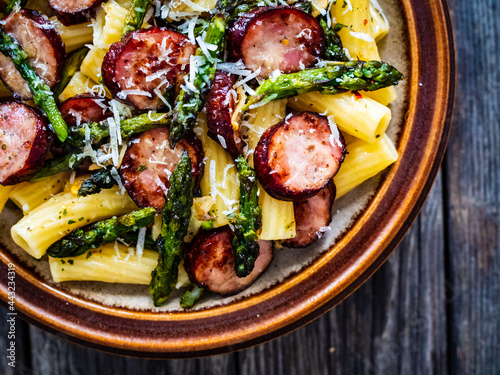 Tortiglioni with sausages, parmesan and asparagus on wooden table 