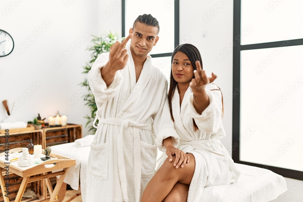 Young latin couple wearing towel standing at beauty center showing middle finger, impolite and rude fuck off expression Young latin couple wearing towel standing at beauty center showing middle finger, impolite and rude fuck off expression