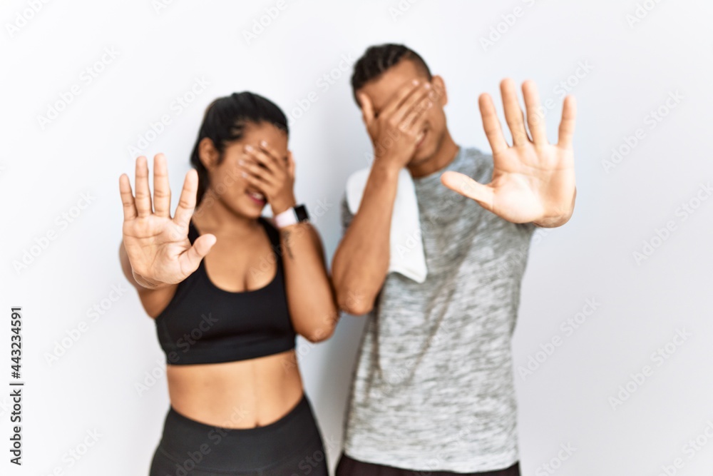 Young latin couple wearing sportswear standing over isolated background covering eyes with hands and doing stop gesture with sad and fear expression. embarrassed and negative concept. Young latin couple wearing sportswear standing over isolated background covering eyes with hands and doing stop gesture with sad and fear expression. embarrassed and negative concept.