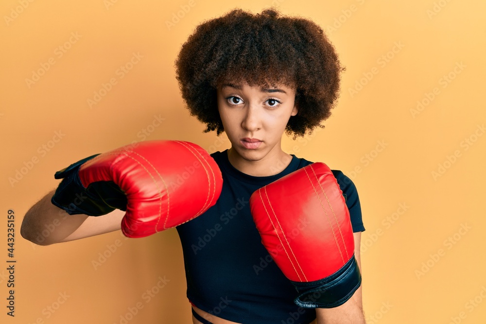 Young hispanic sporty girl using boxing gloves clueless and confused expression. doubt concept.