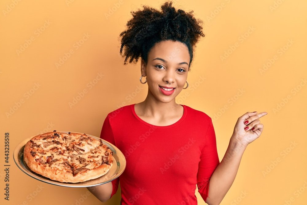 Young african american girl holding italian pizza smiling happy pointing with hand and finger to the side Young african american girl holding italian pizza smiling happy pointing with hand and finger to the side