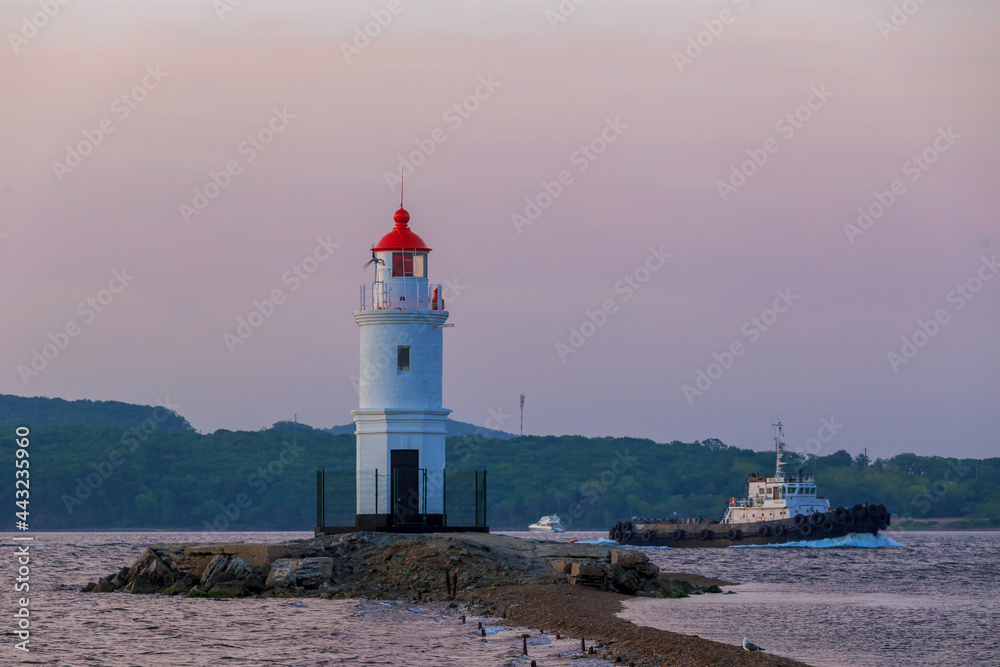 Tokarevsky lighthouse in Vladivostok. Old white lighthouse on the background of the sea and the green island. Marine landmark of the Primorsky region.