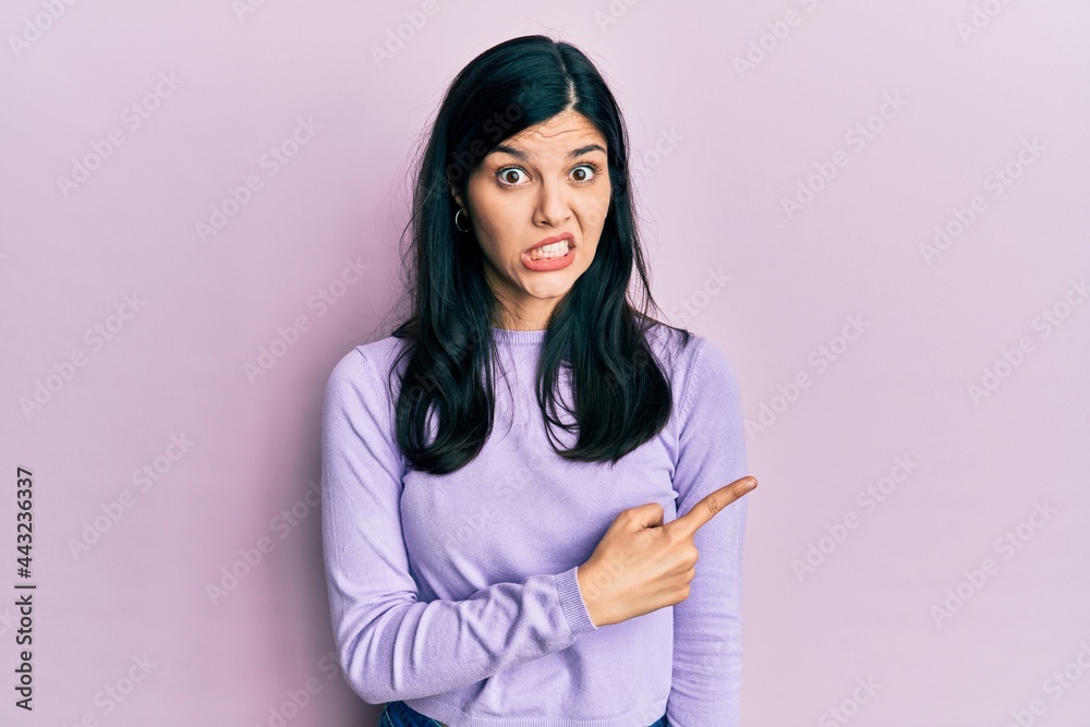 Young hispanic woman wearing casual clothes pointing aside worried and nervous with forefinger, concerned and surprised expression Young hispanic woman wearing casual clothes pointing aside worried and nervous with forefinger, concerned and surprised expression