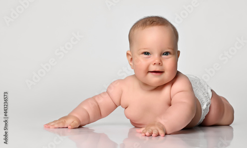 Happy portrait Six month old baby girl in a diaper lying sly looking at you, arms outstretched to the sides. on white background