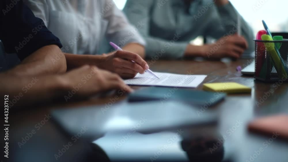 Close-up hands of unrecognizable business woman during team meeting holding pen showing details at paper document at meeting. Closeup of business people discussing business project with colleagues .