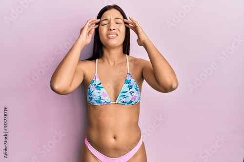 Young latin woman wearing bikini suffering from headache desperate and stressed because pain and migraine. hands on head.