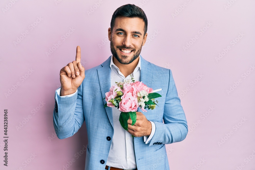 Young hispanic businessman wearing business jacket holding flowers surprised with an idea or question pointing finger with happy face, number one Young hispanic businessman wearing business jacket holding flowers surprised with an idea or question pointing finger with happy face, number one