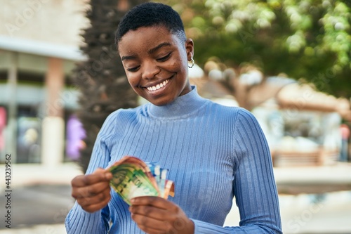 Fotografia Young african american woman smiling happy counting south africa rand banknotes at the city