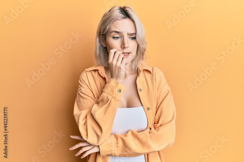 Young blonde girl wearing casual clothes looking stressed and nervous with hands on mouth biting nails. anxiety problem.