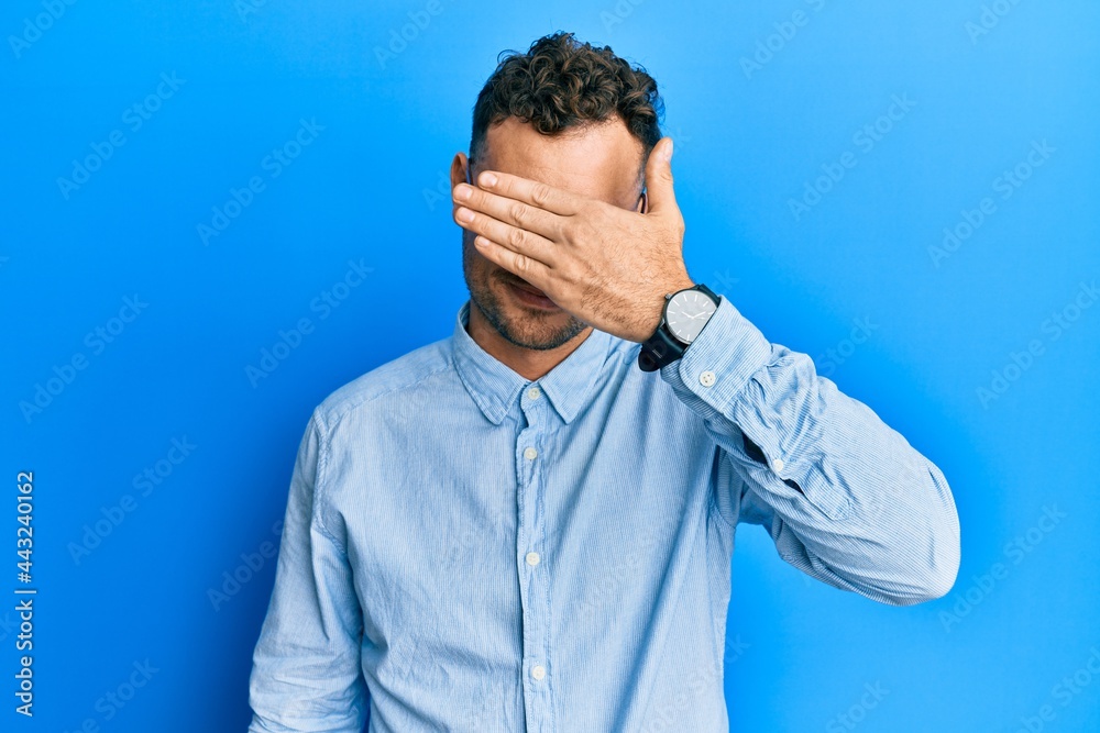 Young hispanic man wearing casual clothes and glasses covering eyes with hand, looking serious and sad. sightless, hiding and rejection concept