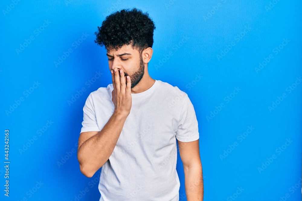 Young arab man with beard wearing casual white t shirt bored yawning tired covering mouth with hand. restless and sleepiness.