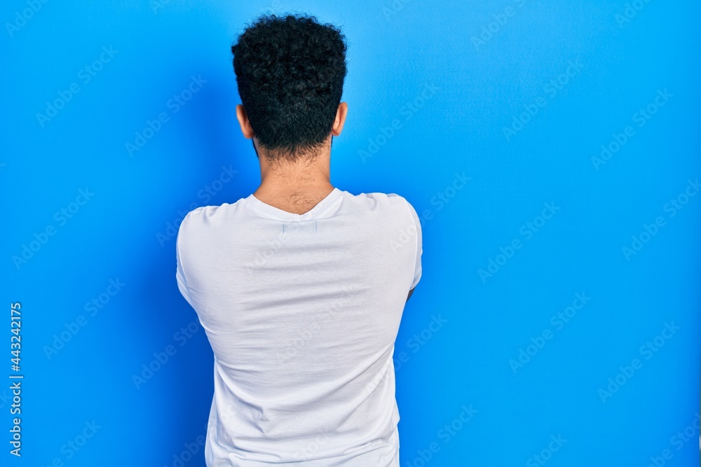 Young arab man with beard wearing casual white t shirt standing backwards looking away with crossed arms Young arab man with beard wearing casual white t shirt standing backwards looking away with crossed arms