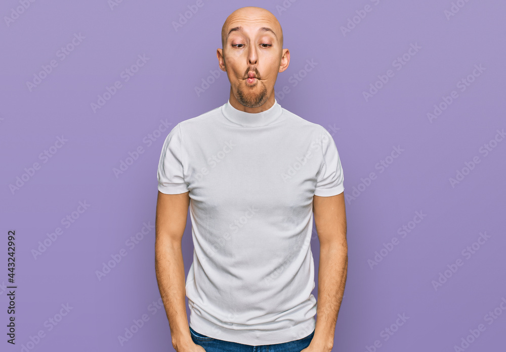 Bald man with beard wearing casual white t shirt making fish face with lips, crazy and comical gesture. funny expression. Bald man with beard wearing casual white t shirt making fish face with lips, crazy and comical gesture. funny expression.