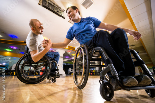 Two young disabled men in wheelchairs playing bowling in the club