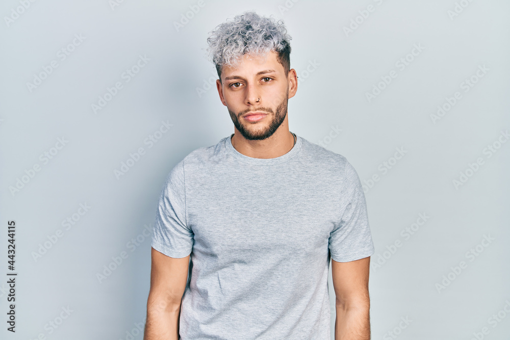 Young hispanic man with modern dyed hair wearing casual grey t shirt relaxed with serious expression on face. simple and natural looking at the camera. Young hispanic man with modern dyed hair wearing casual grey t shirt relaxed with serious expression on face. simple and natural looking at the camera.