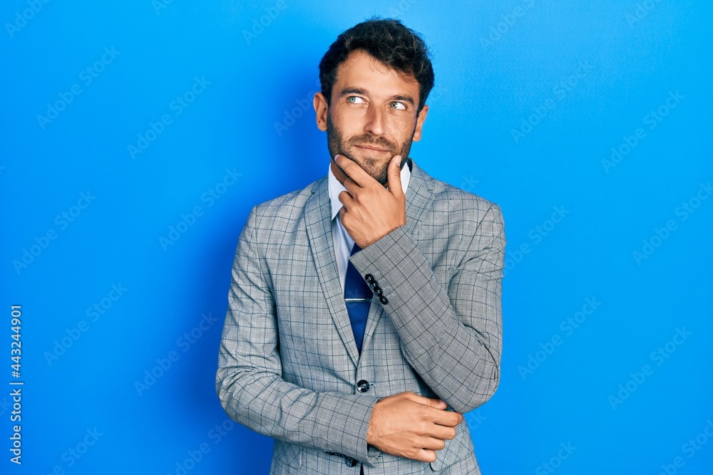Handsome man with beard wearing business suit and tie with hand on chin thinking about question, pensive expression. smiling with thoughtful face. doubt concept. Handsome man with beard wearing business suit and tie with hand on chin thinking about question, pensive expression. smiling with thoughtful face. doubt concept.