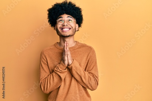 Young african american man with afro hair wearing casual winter sweater begging and praying with hands together with hope expression on face very emotional and worried. begging. © Krakenimages.com