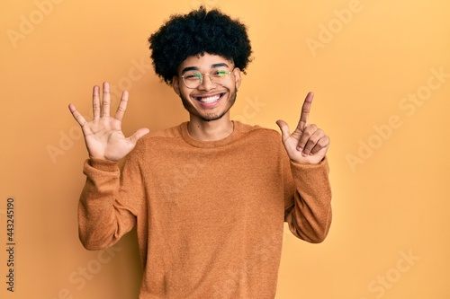 Young african american man with afro hair wearing casual winter sweater showing and pointing up with fingers number seven while smiling confident and happy.