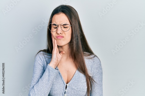 Young brunette teenager wearing casual sweater and glasses touching mouth with hand with painful expression because of toothache or dental illness on teeth. dentist