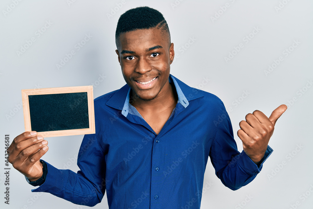 Young african american man holding empty frame pointing thumb up to the side smiling happy with open mouth Young african american man holding empty frame pointing thumb up to the side smiling happy with open mouth
